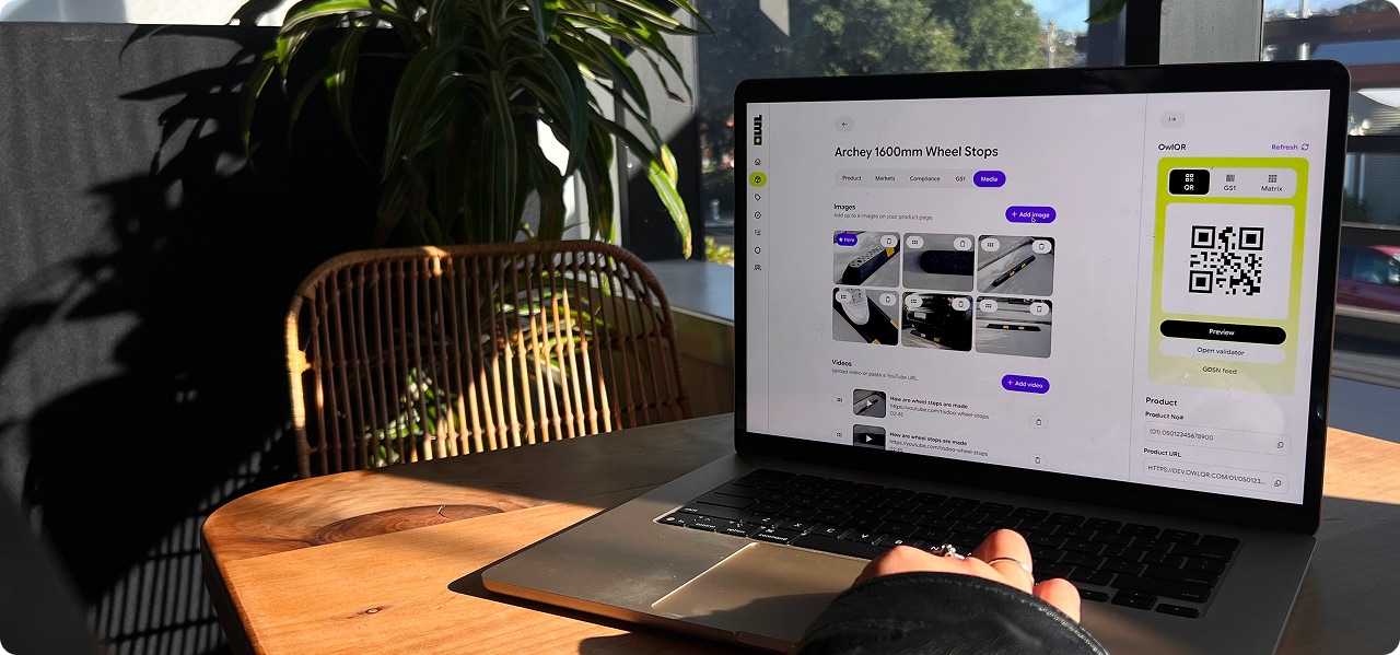 A laptop on a sunlit desk showing an OwlQR product page for Archey 1600mm wheel stops, with its GS1 QR code ready to publish.
